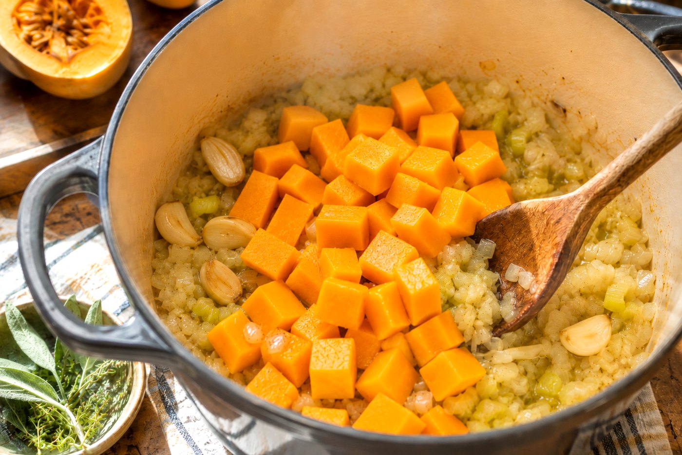 Butternut squash added to gently softened aromatics and golden garlic in a Dutch oven.